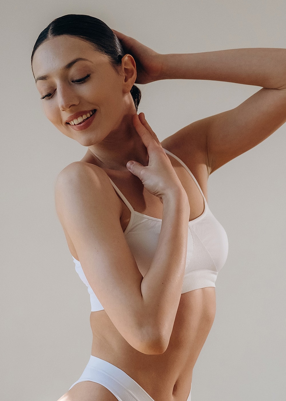 Smiling woman in white lingerie against neutral background.