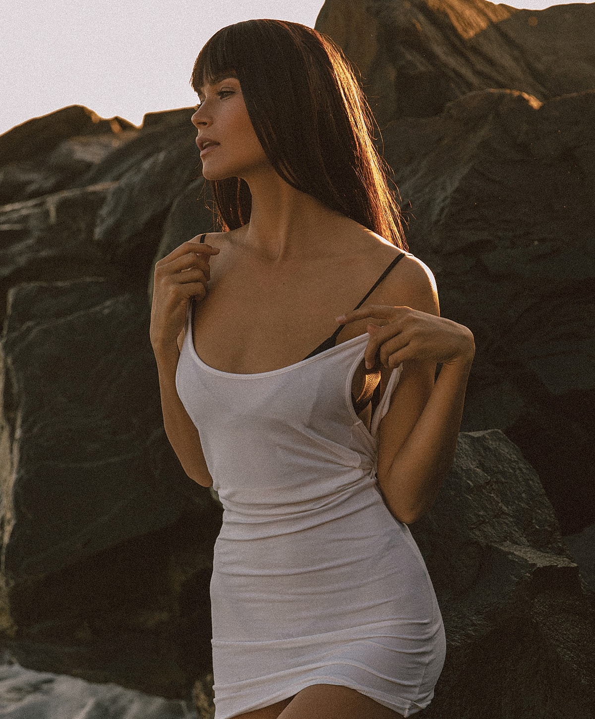 extended tummy tuck patient model in a white dress by rocky shoreline.