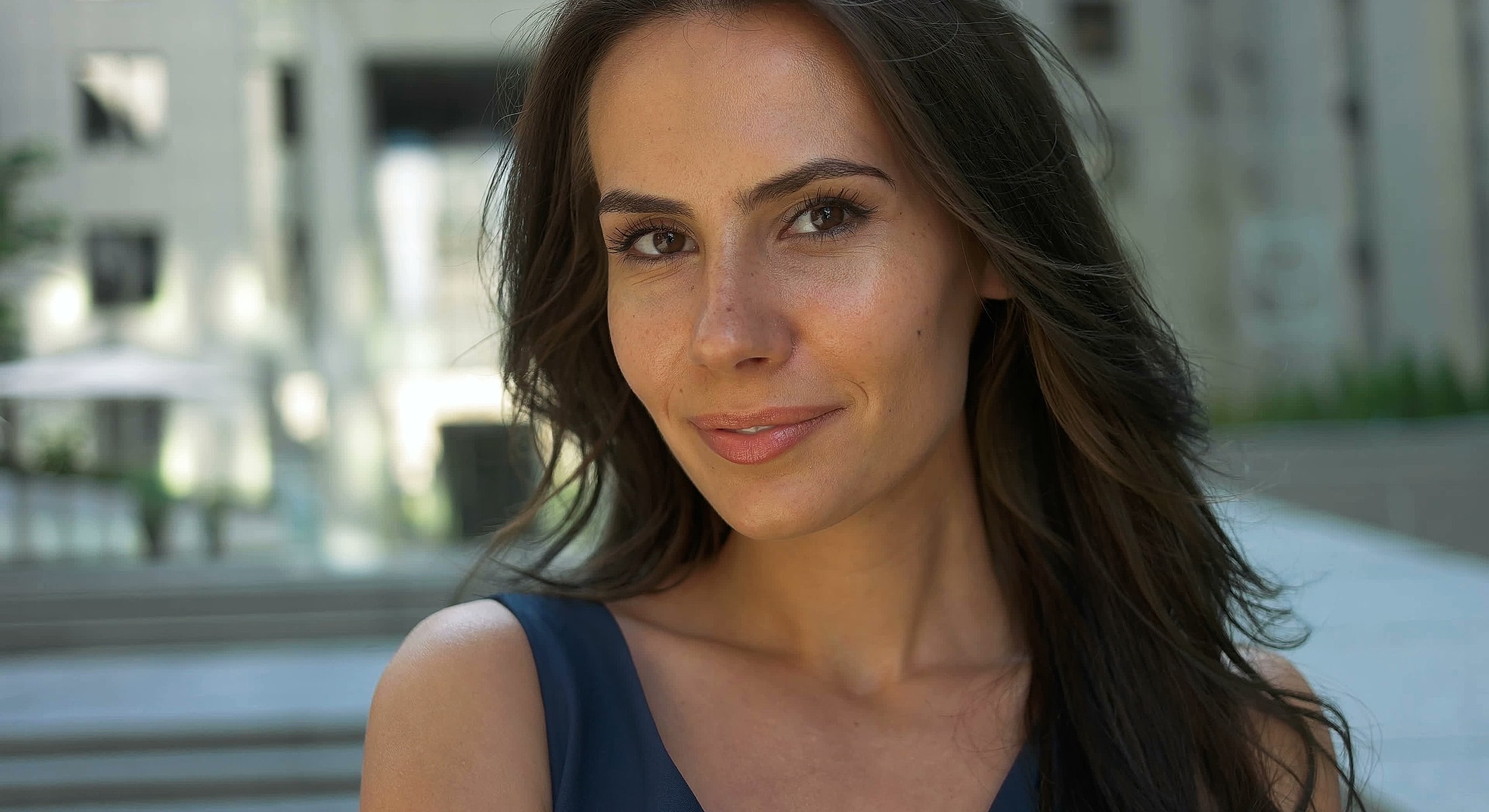 Smiling woman outdoors with long, wavy hair.