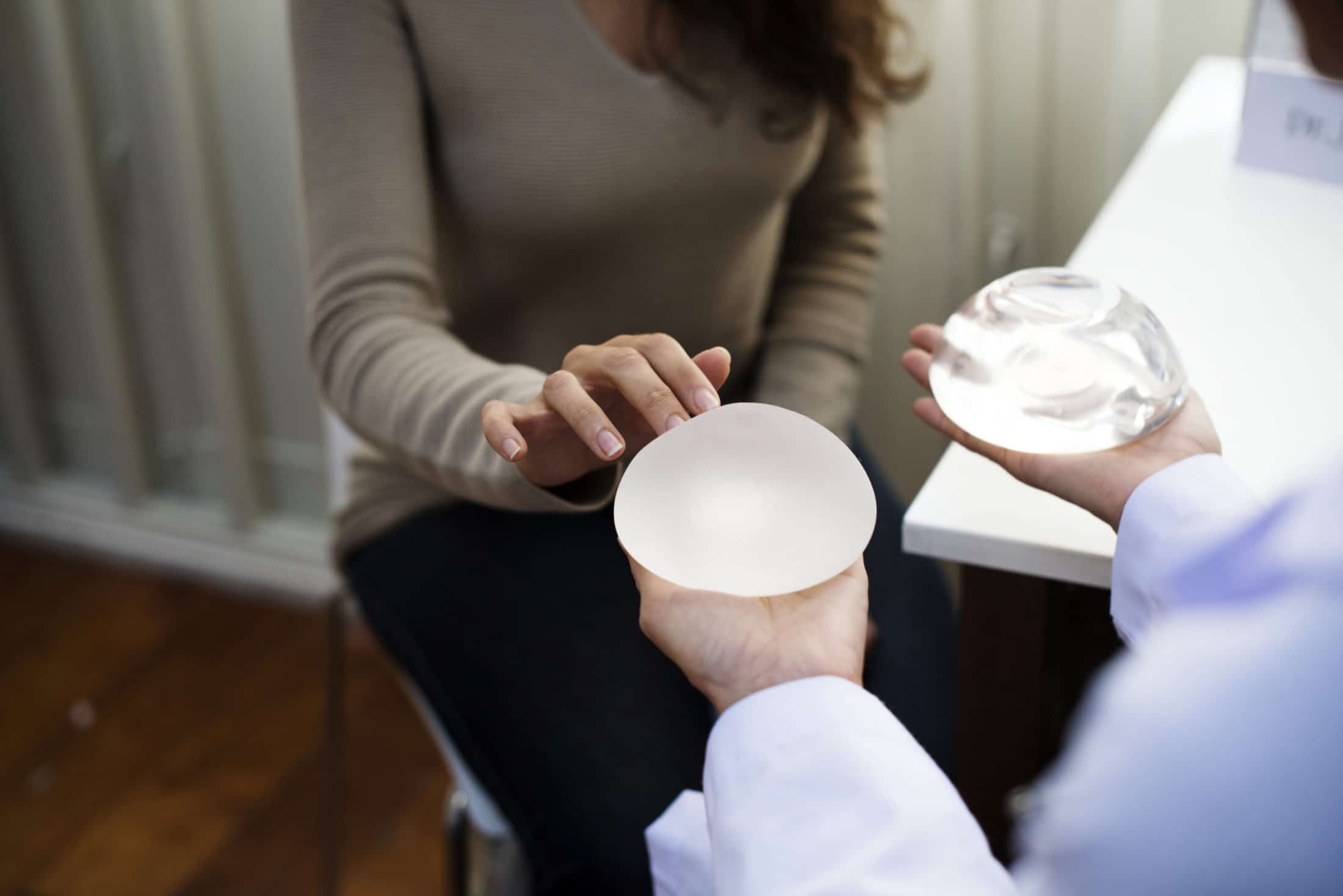 doctor holding out two breast implants showing patient, one saline, one silicone