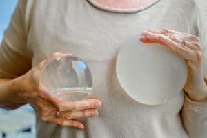A woman holding two silicone breast implants against her chest.